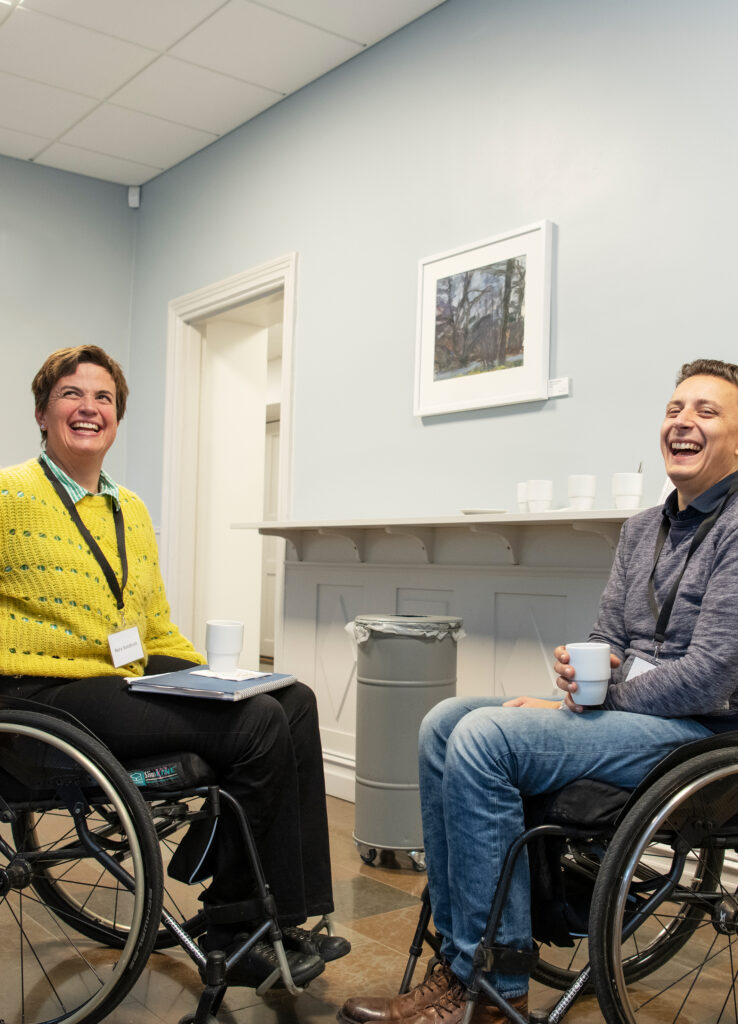 En kvinna och en man i rullstol skrattar och är glada medan de fikar